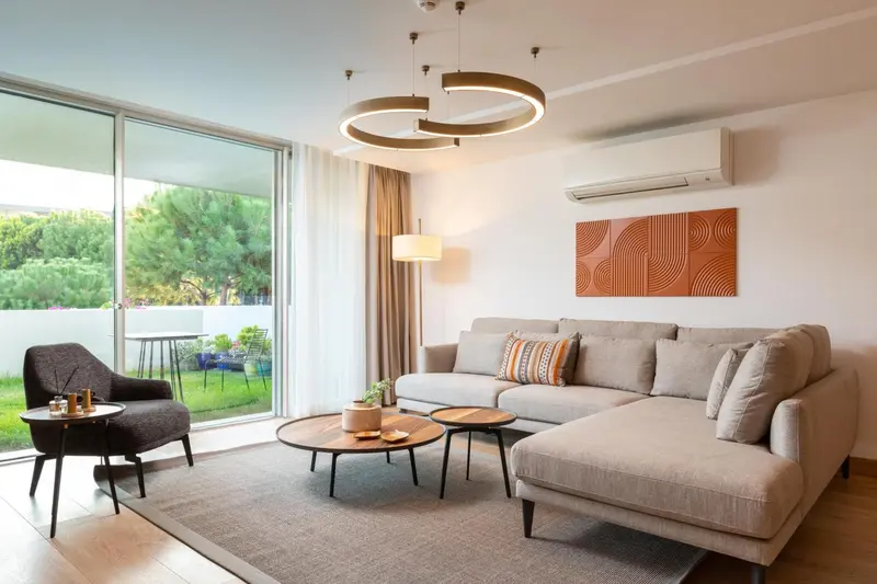 Un salon moderne avec canapé d'angle et fauteuil près d'une grande baie vitrée.