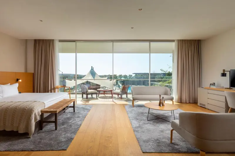 Une chambre lumineuse avec un grand lit et un coin salon donnant sur une vue extérieure.