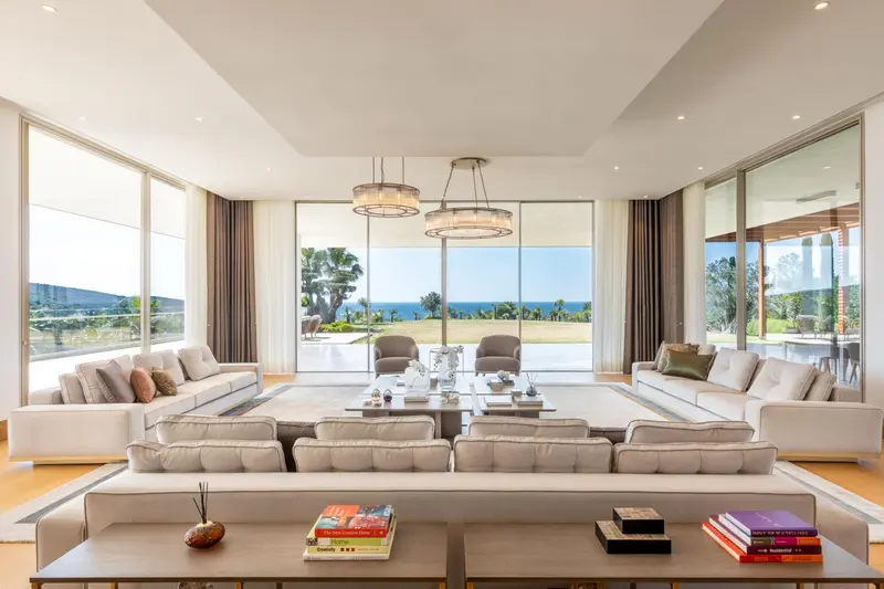 Vaste salon moderne avec de larges baies vitrées donnant sur la mer.