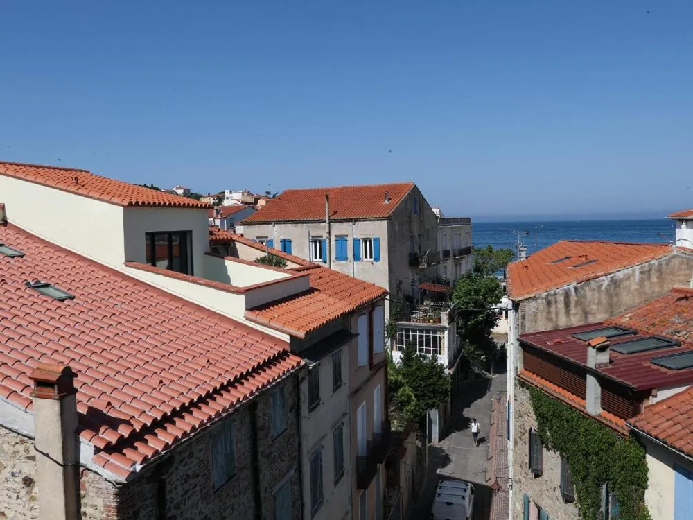 Vue aérienne sur des toits de tuiles rouges et des bâtiments méditerranéens avec la mer en arrière-plan.