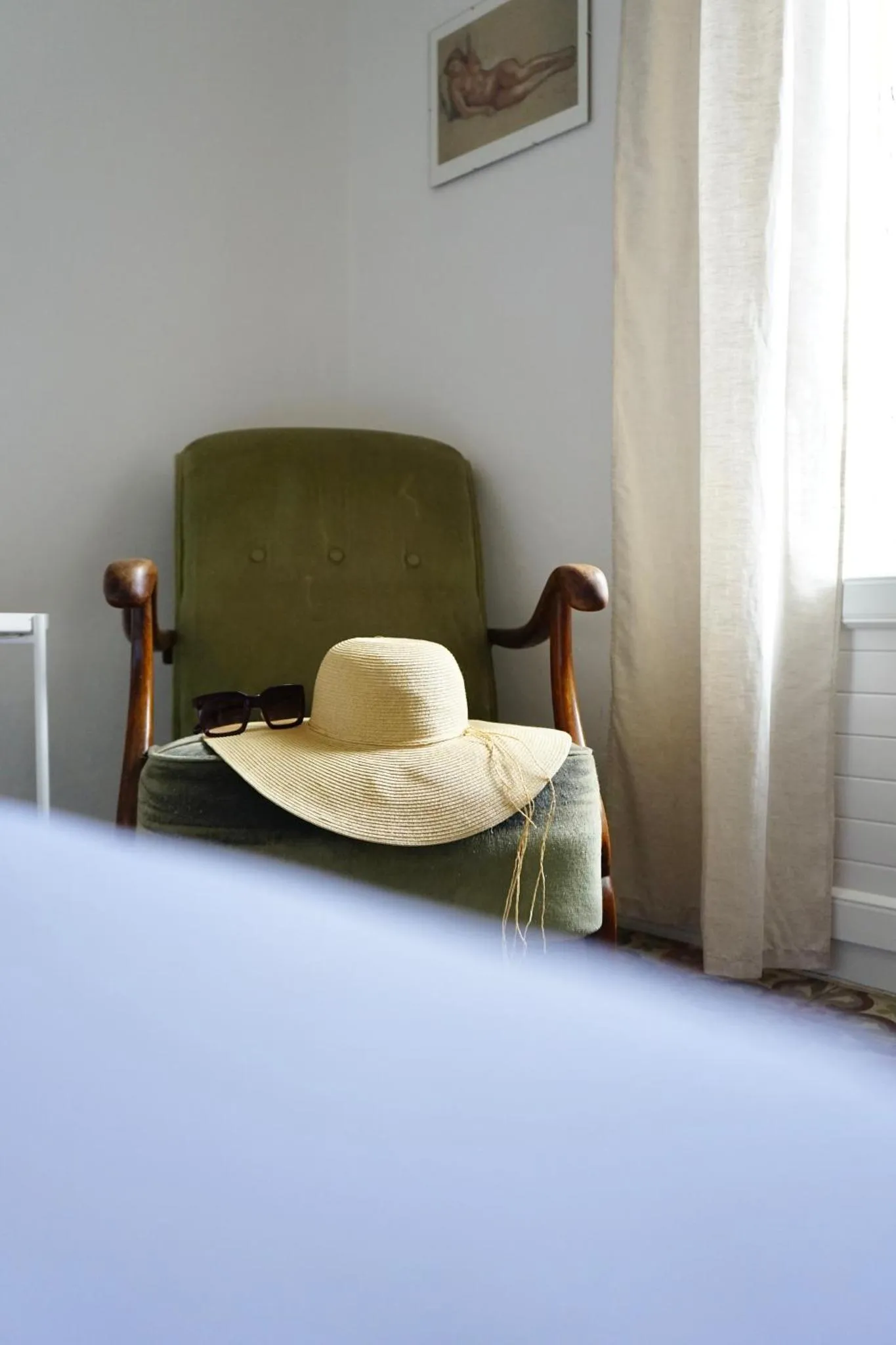 Un chapeau de paille et des lunettes de soleil reposent sur un fauteuil vert.