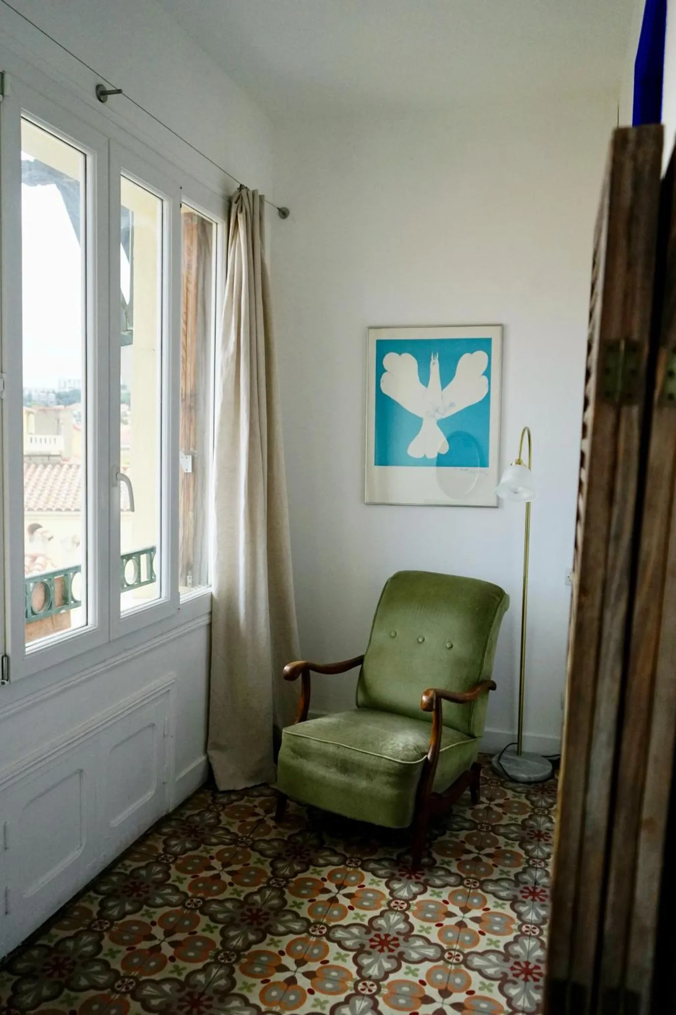 Une chaise verte est placée près d'une fenêtre dans une pièce lumineuse.