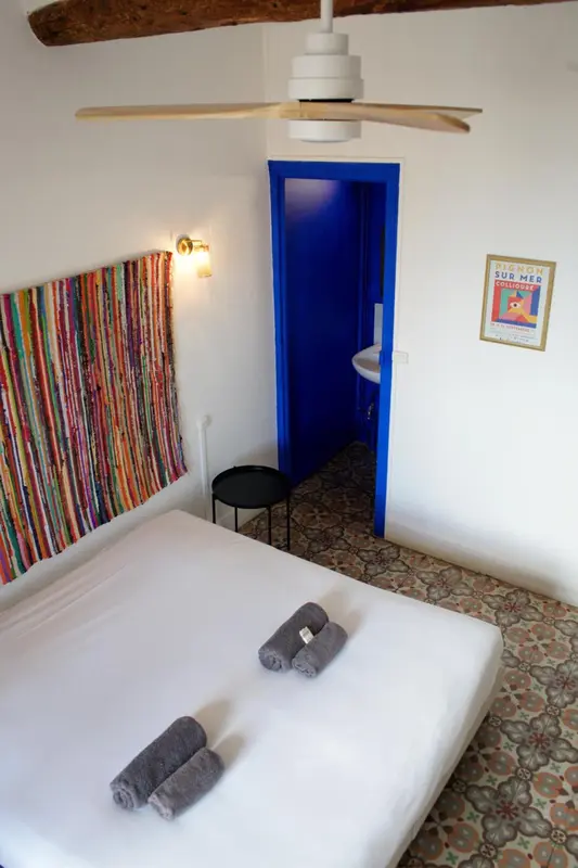 Une chambre lumineuse avec un lit recouvert d'un drap blanc et un rideau coloré.