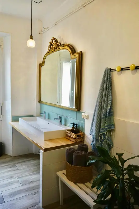 Une salle de bain lumineuse avec un grand miroir doré et une vasque blanche.