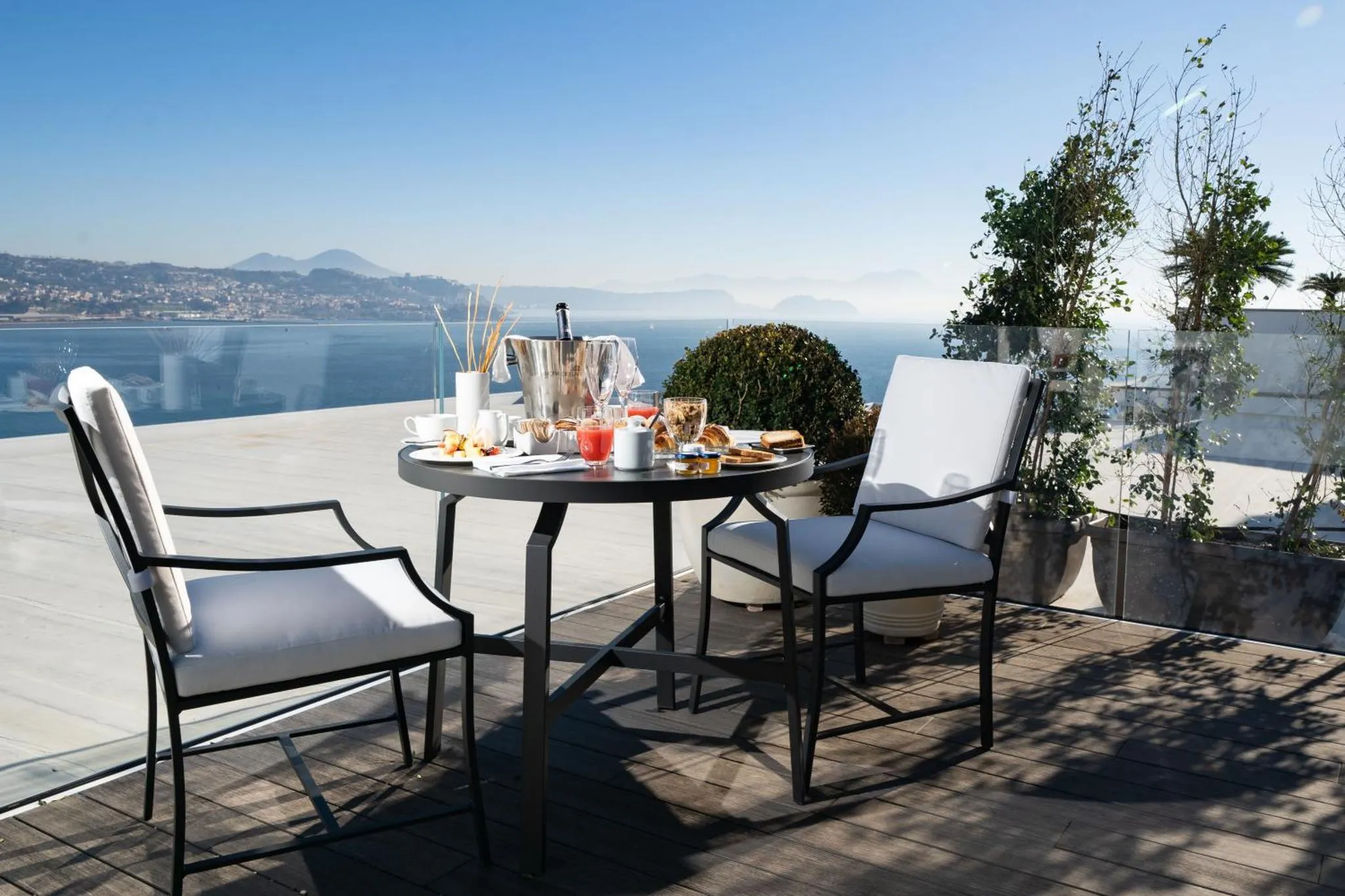 Une table ronde est dressée sur une terrasse avec vue sur la mer et les montagnes.