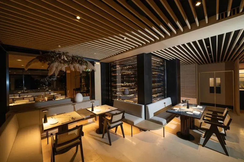 Une salle de restaurant moderne avec des tables éclairées et un bar à vin en arrière-plan.