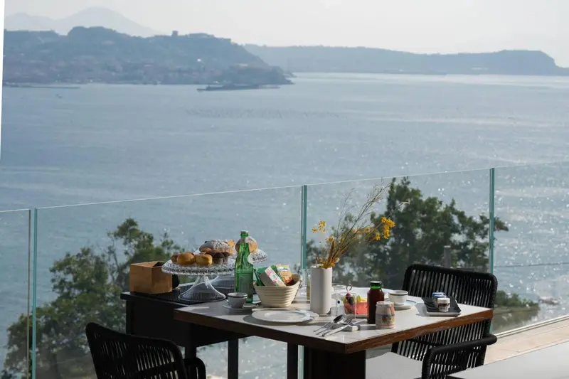 Une table de petit-déjeuner est dressée sur une terrasse avec vue sur la mer.
