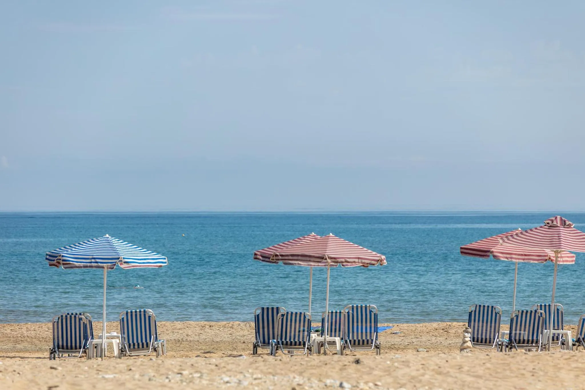 Transats rayés sous des parasols sur une plage de sable fin face à la mer.