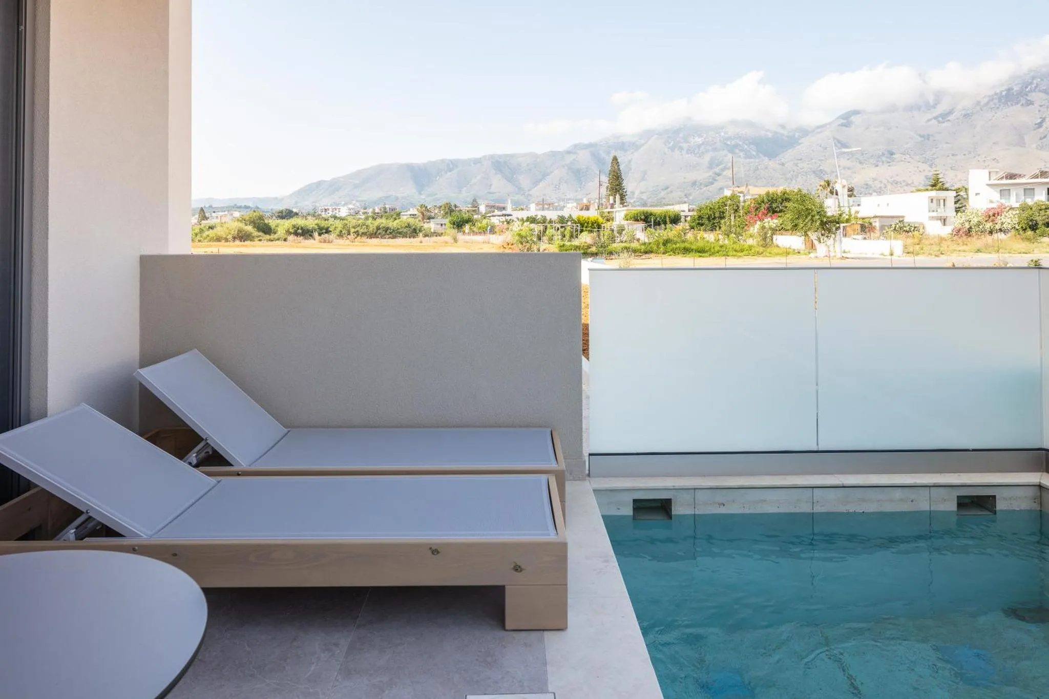 Deux transats blancs sur une terrasse avec une petite piscine et une vue sur les montagnes.