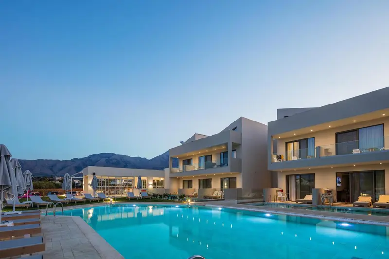 Vue d'une piscine devant un bâtiment moderne avec des montagnes en arrière-plan.