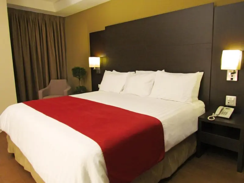Une chambre d'hotel avec un grand lit recouvert d'une courtepointe rouge et de coussins blancs.