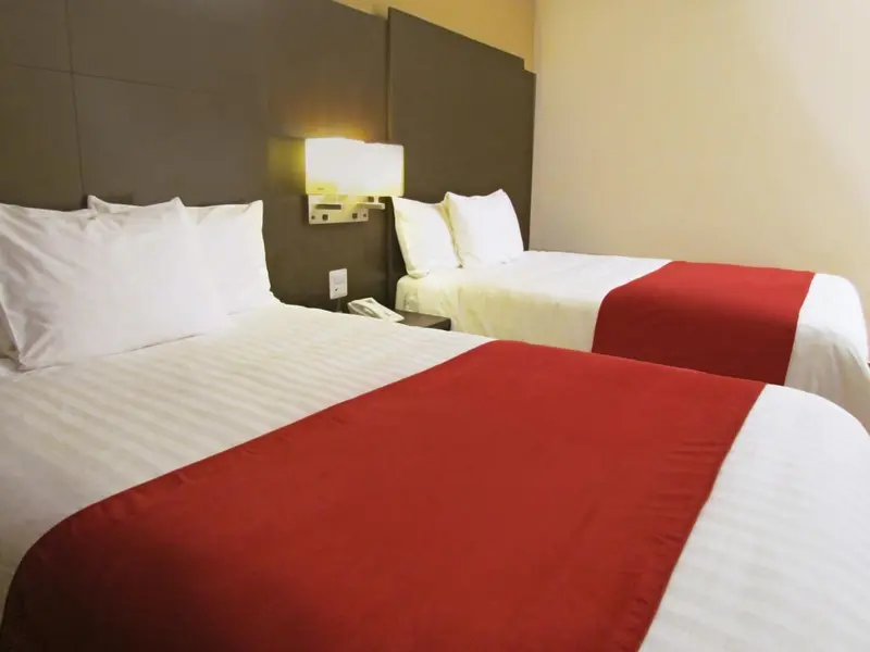 Deux lits simples avec une couverture rouge et des oreillers blancs dans une chambre.