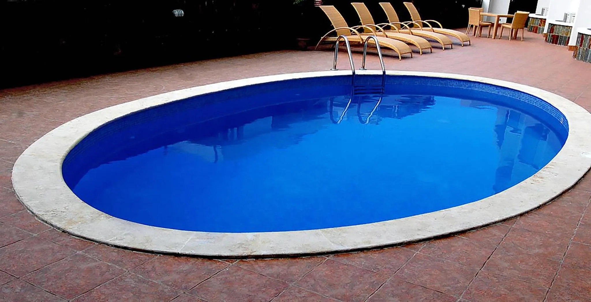 Une piscine rectangulaire bleue entourée d'une terrasse carrelée.