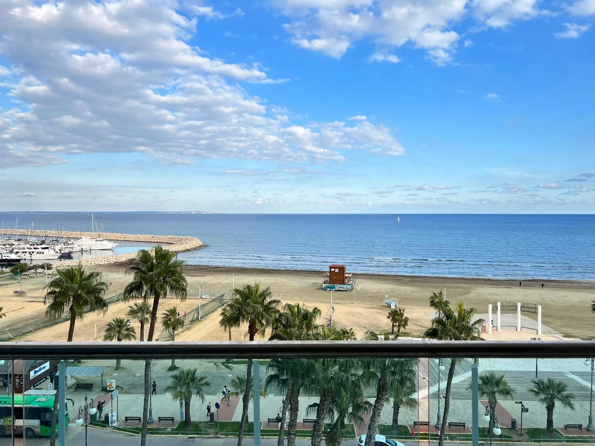Vue sur la mer depuis un balcon avec des palmiers et une promenade.