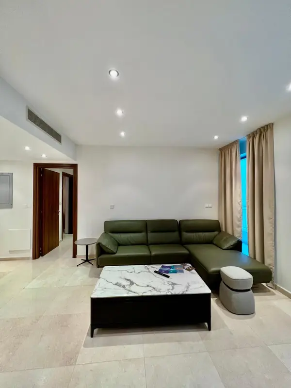 Un salon clair avec un canapé vert et une table basse en marbre.