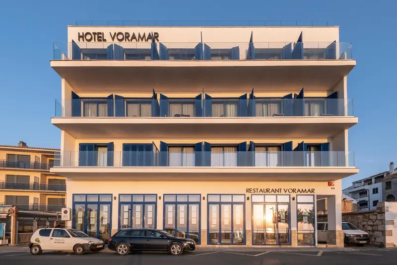Façade d'un bâtiment blanc à plusieurs étages avec des balcons bleus et une entrée vitrée.