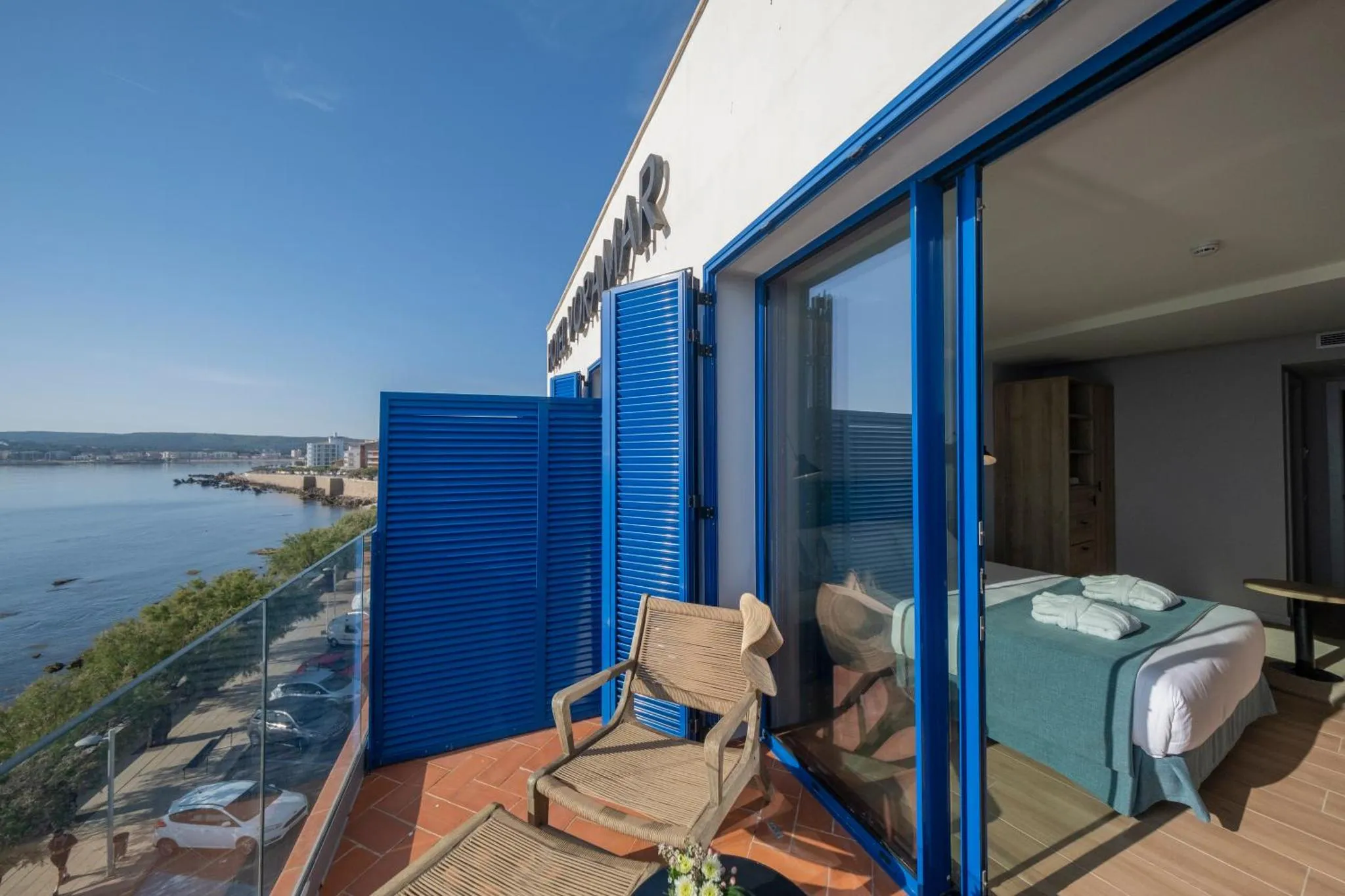 Une terrasse avec une vue sur la mer et un lit visible à travers les baies vitrées.