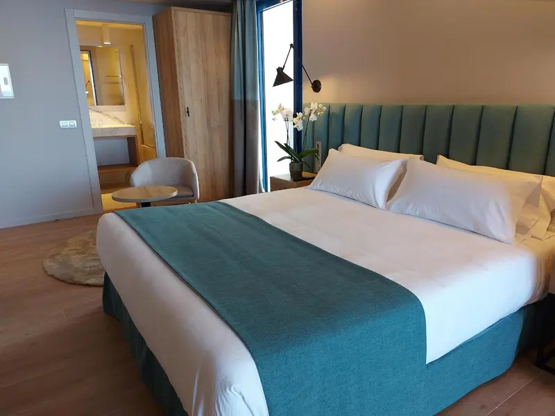 Une chambre lumineuse avec un grand lit recouvert d'une courtepointe turquoise.
