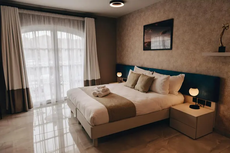 Une chambre lumineuse avec un grand lit et un accès à un balcon.