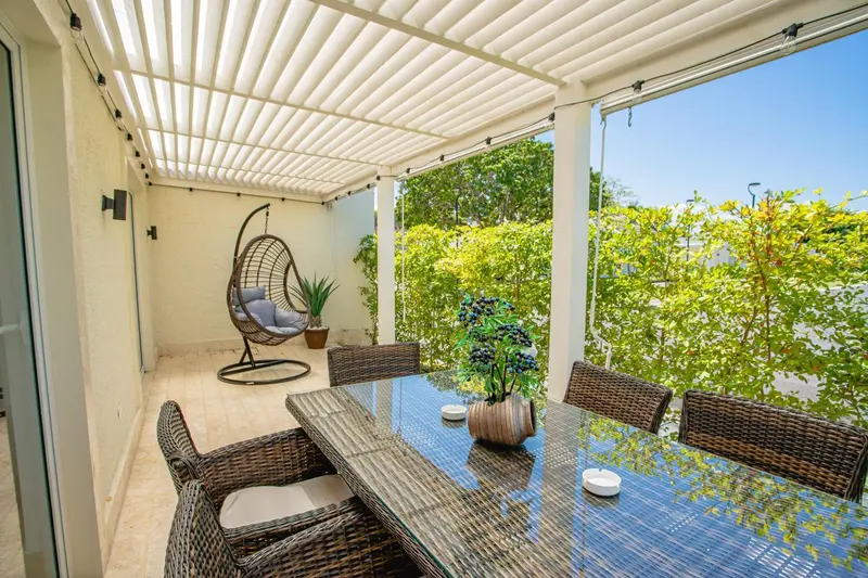 Une table à manger en osier est placée sur une terrasse couverte.