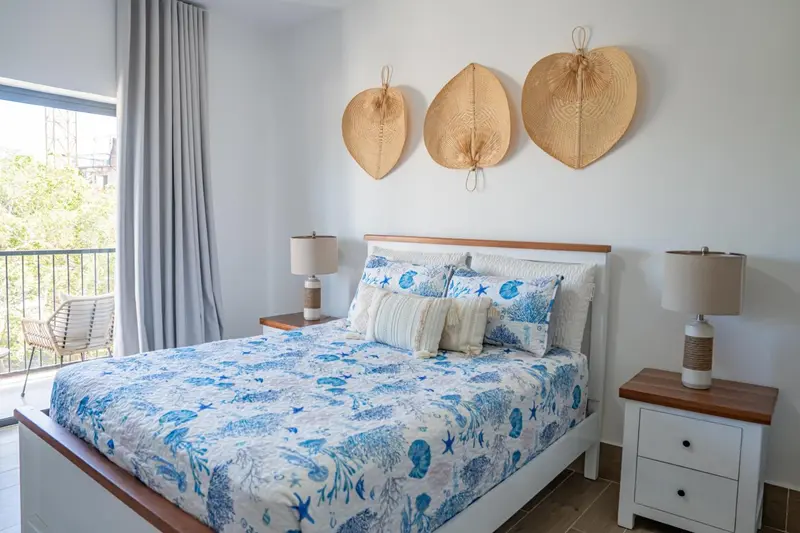 Une chambre lumineuse avec un grand lit décoré de motifs marins et un balcon.
