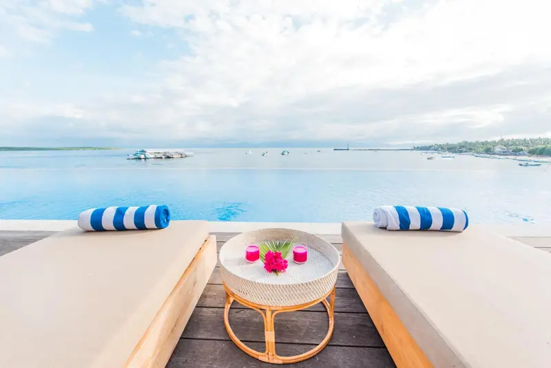 Deux transats et une table basse sur une terrasse en bois avec vue sur la mer.