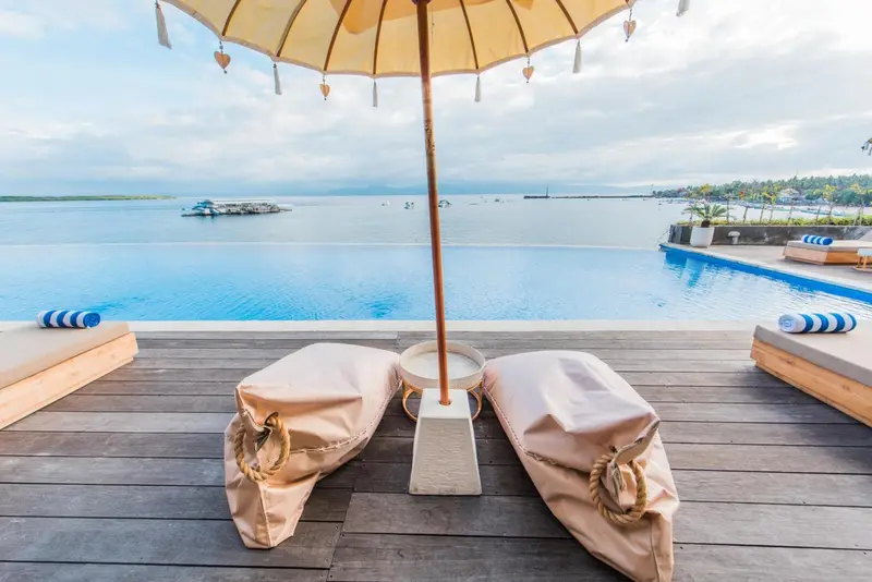 Transats et parasol au bord d'une piscine à débordement avec vue sur la mer.