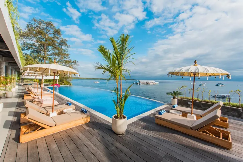 Transats et parasols bordent une piscine à débordement avec vue sur la mer.