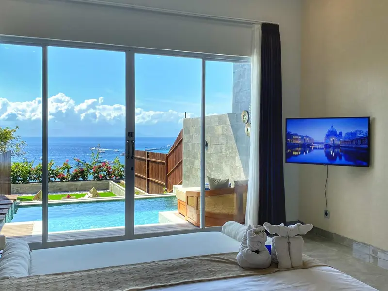 Une chambre lumineuse s'ouvre sur une piscine et une vue sur la mer.