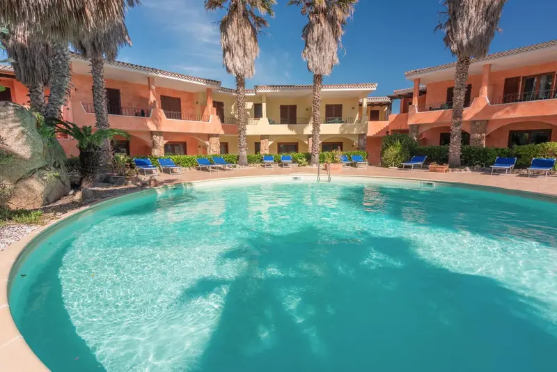 Piscine turquoise bordée de chaises longues et de palmiers.