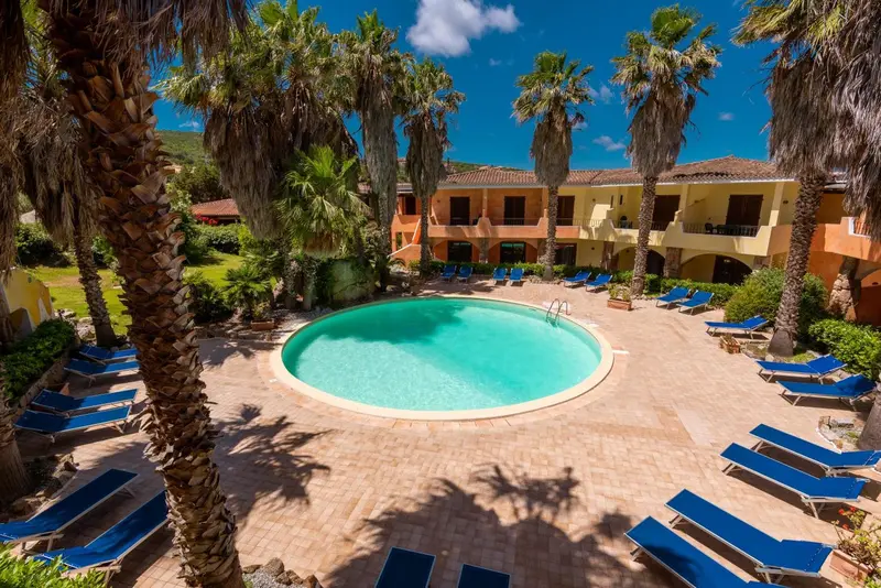Une piscine rectangulaire entourée de transats bleus et de palmiers.