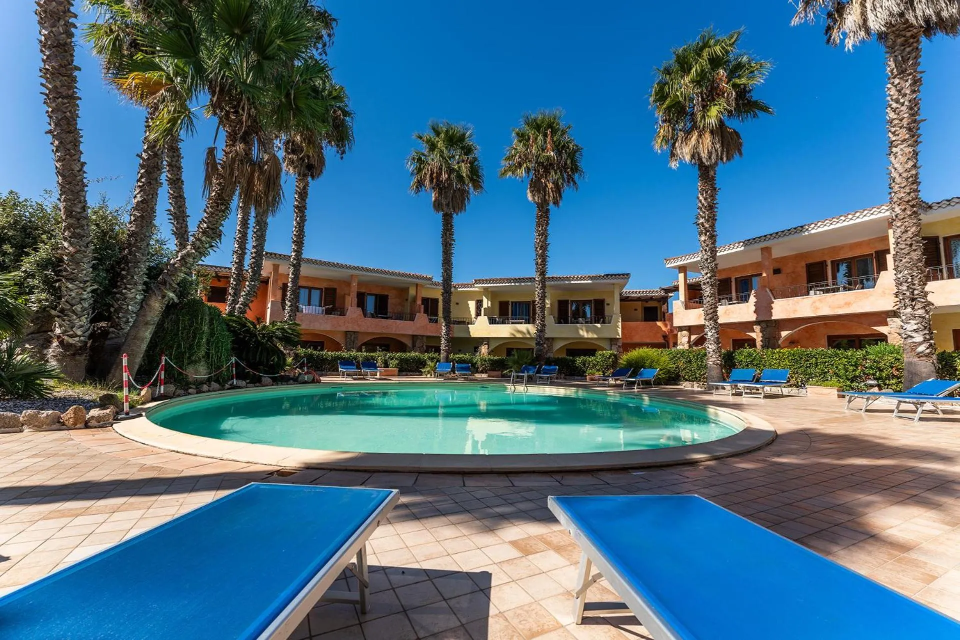 Transats bleus disposés autour d'une piscine rectangulaire dans un jardin tropical.