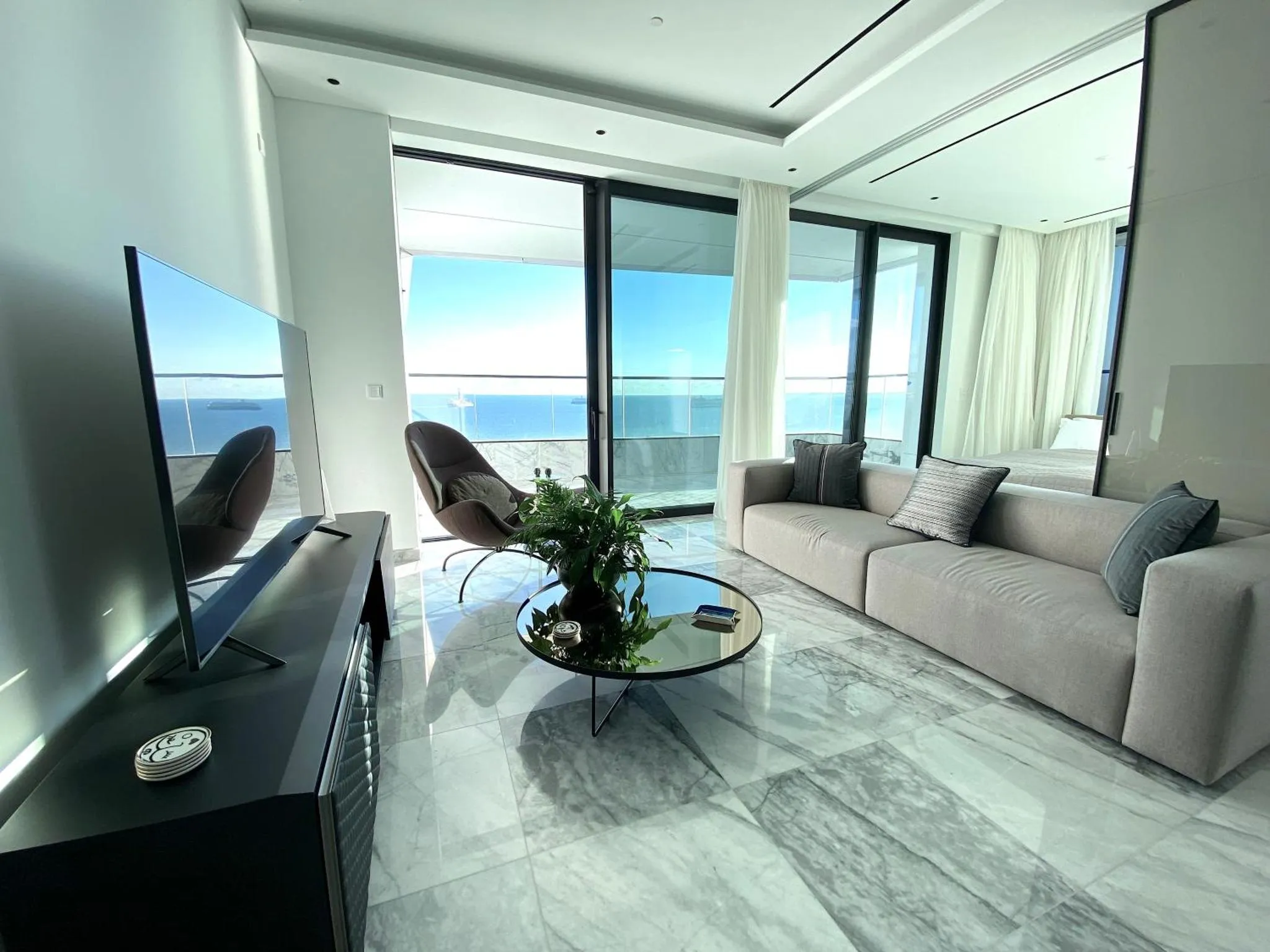 Un espace de détente intérieur avec canapés et télévision face à une baie vitrée donnant sur la mer.