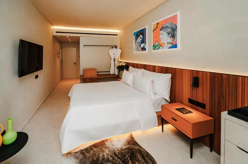 Une chambre lumineuse avec un grand lit recouvert d'une courtepointe blanche et des tableaux colorés.