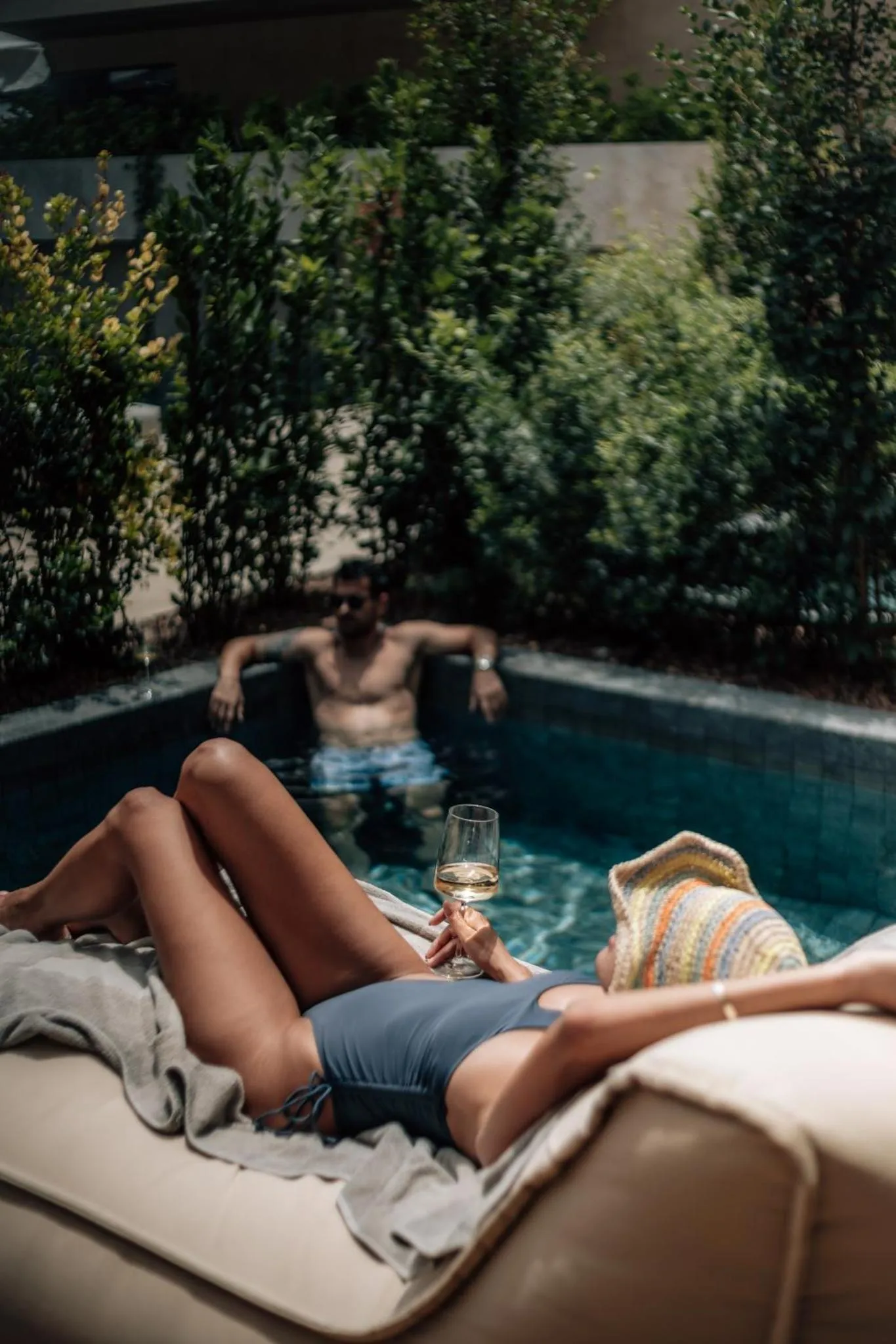 Une personne se détend au bord d'une piscine avec un verre à la main.