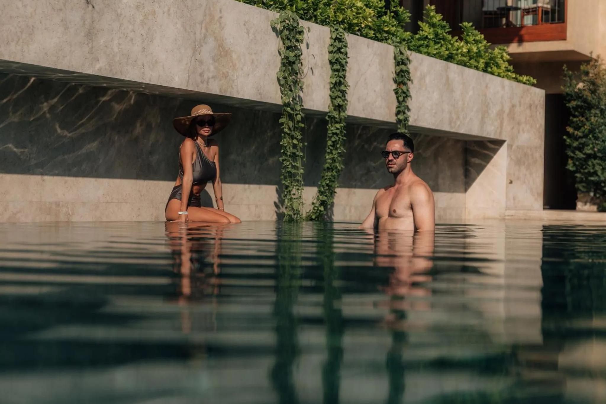 Deux personnes se détendent dans une piscine bordée de végétation.