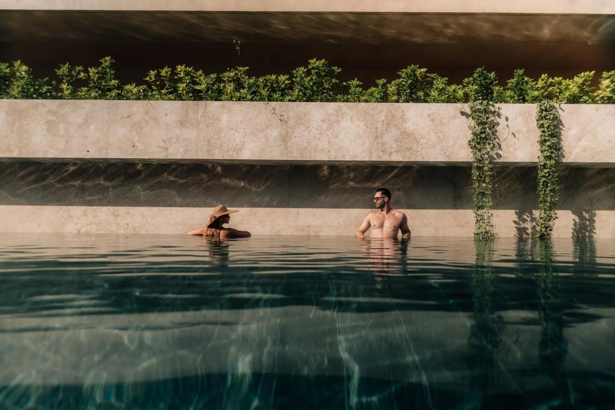 Deux personnes se détendent dans une piscine bordée de végétation.