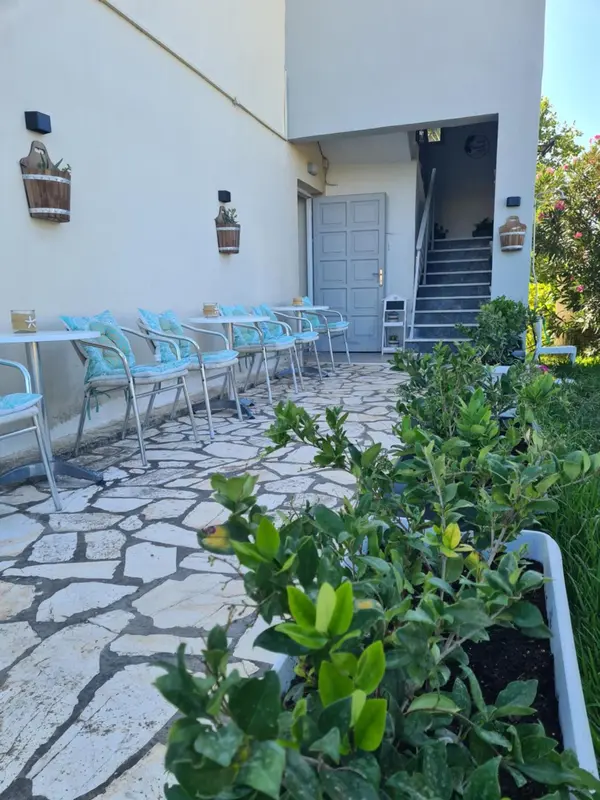 Terrasse pavée avec tables et chaises bleues, devant un bâtiment blanc.