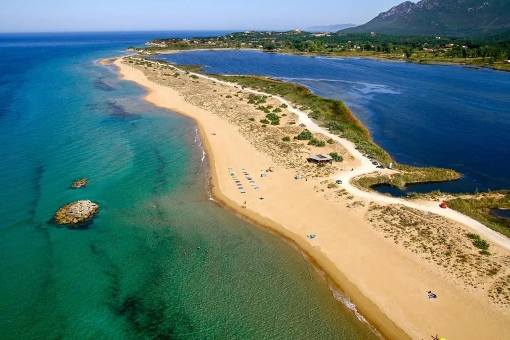 Vue aérienne d'une plage de sable fin bordée d'eau turquoise et de végétation.