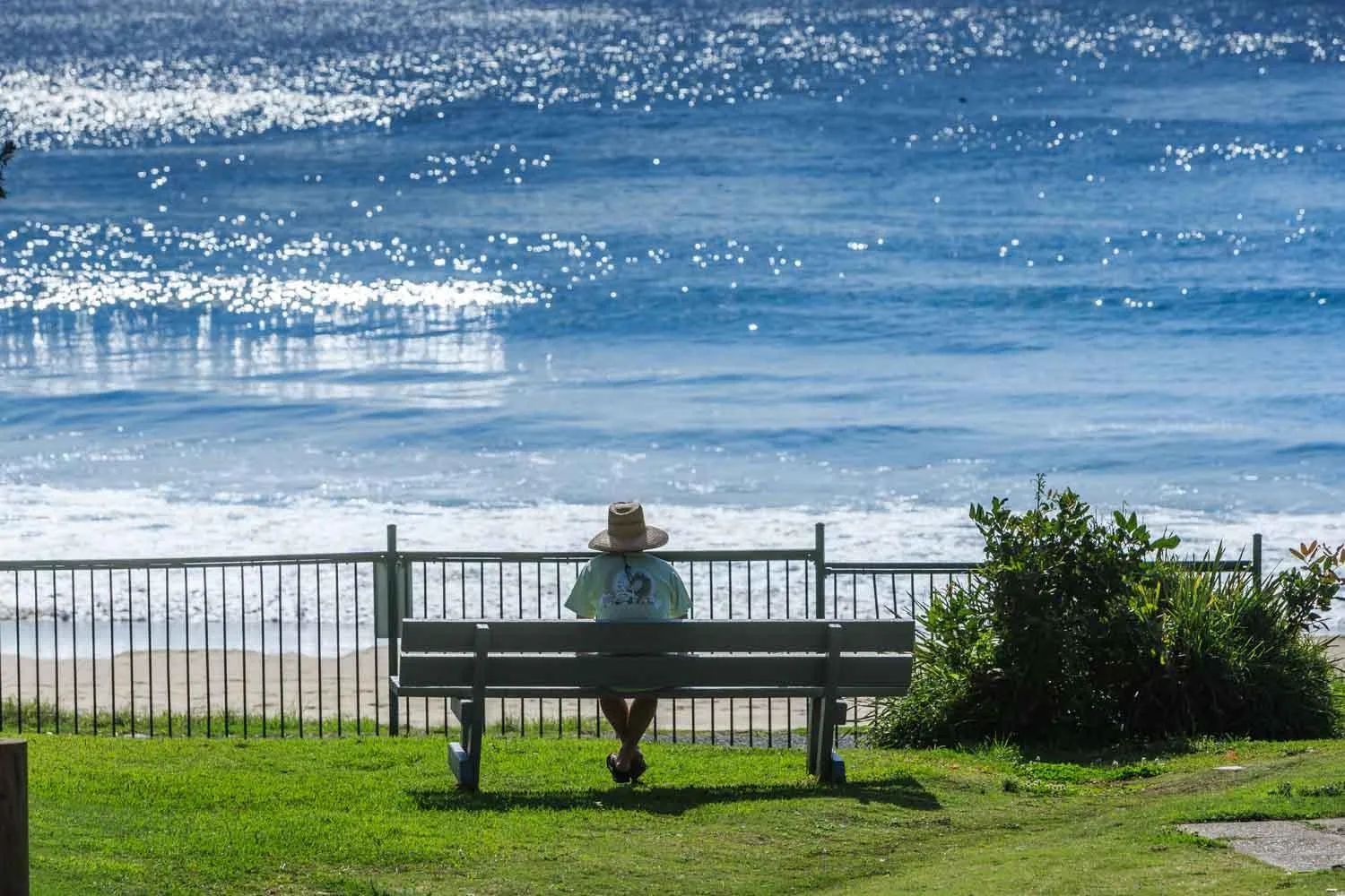 Une personne assise sur un banc face à la mer.