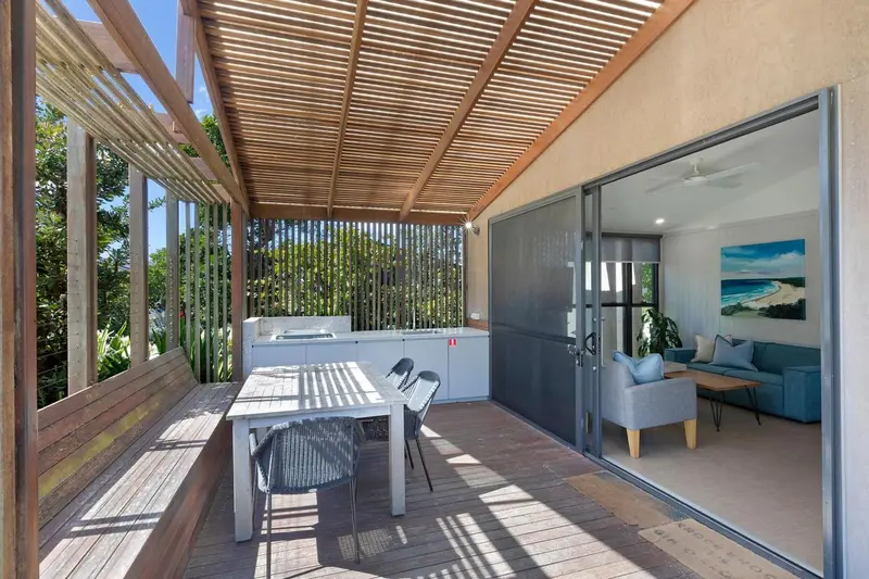 Terrasse en bois avec table et cuisine d'été donnant sur un salon lumineux.