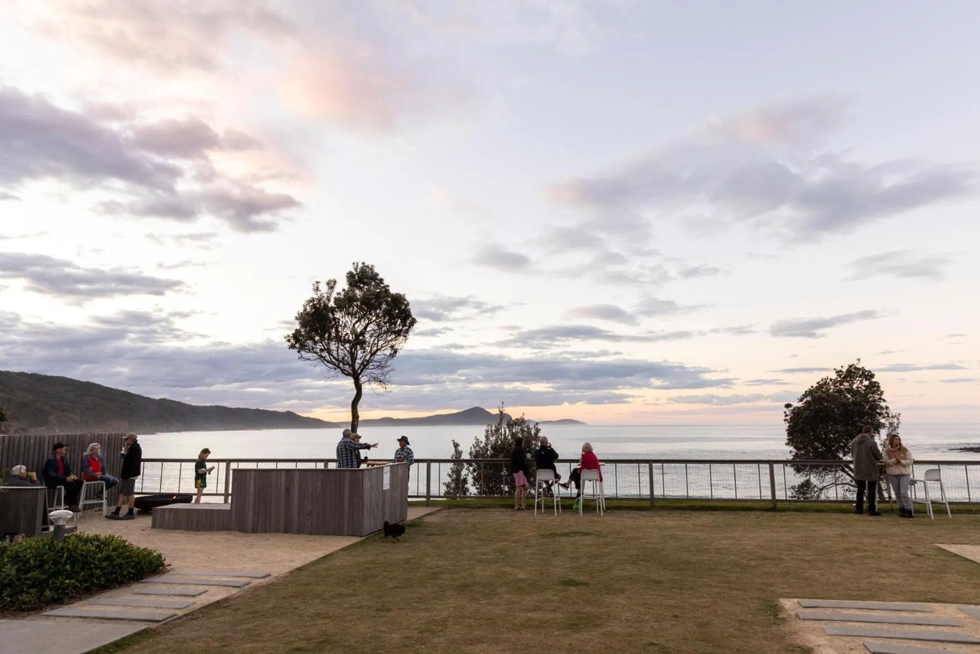 Des personnes se rassemblent sur une terrasse surplombant la mer au coucher du soleil.