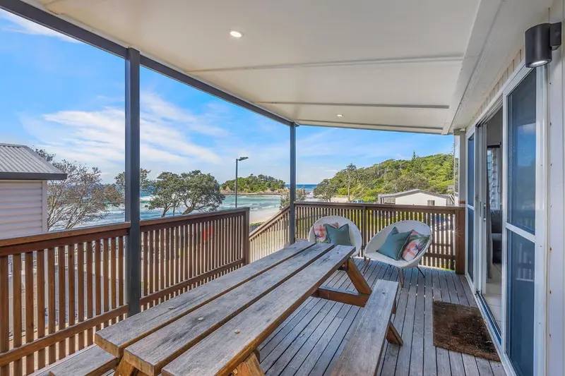 Terrasse en bois avec table et chaises donnant sur une plage et la mer.