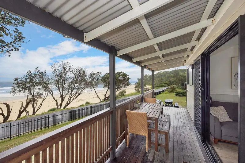 Terrasse en bois avec mobilier d'extérieur donnant sur une plage de sable et la mer.