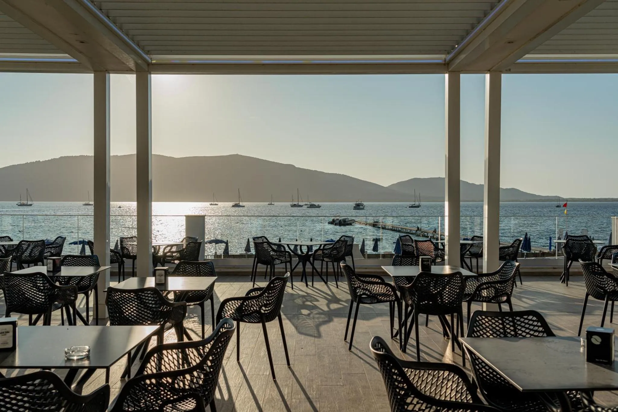 Terrasse ombragée avec tables et chaises donnant sur la mer.
