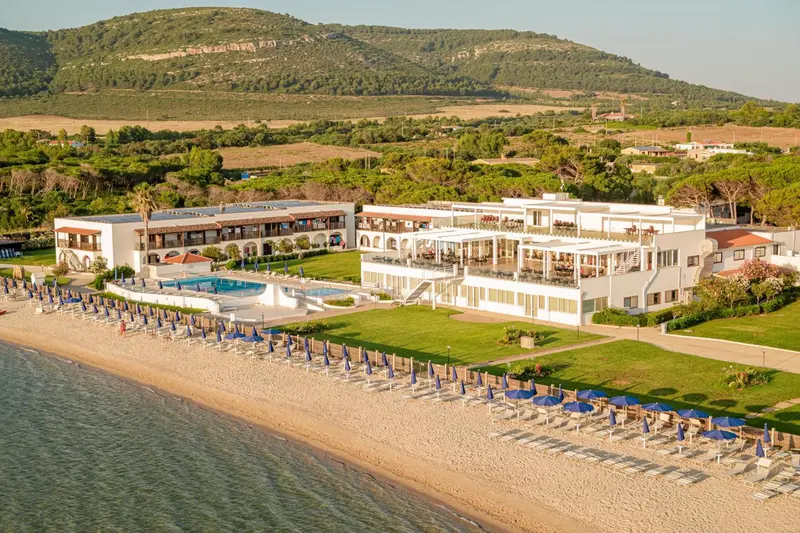 Vue aérienne d'un complexe hôtelier blanc avec piscine et plage de sable.