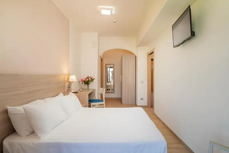 Une chambre lumineuse avec un lit blanc et un bureau.