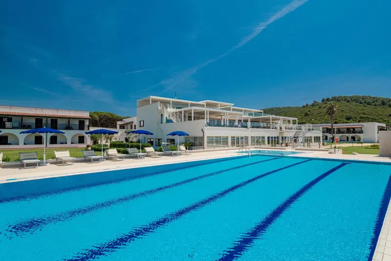 Vue d'une piscine devant un bâtiment blanc sous un ciel bleu.