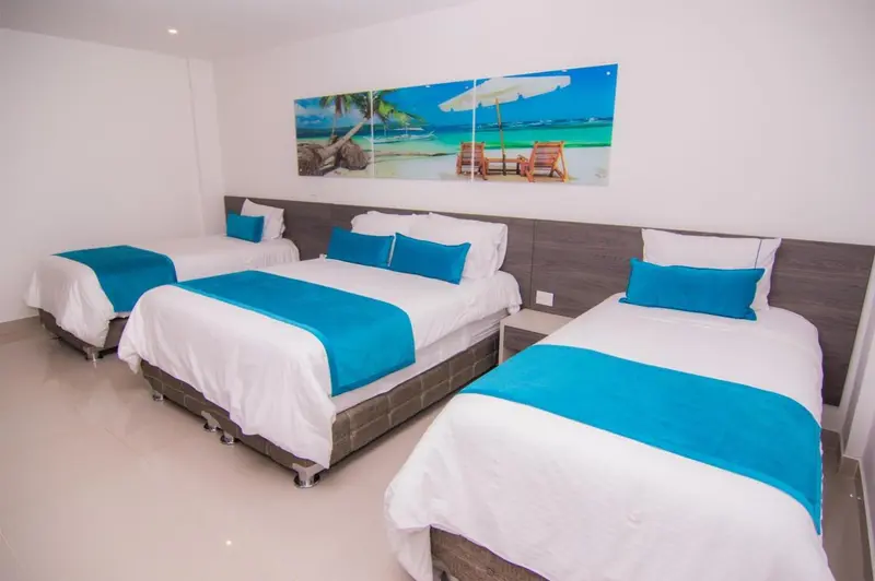 Chambre lumineuse avec trois lits simples et une décoration murale tropicale.