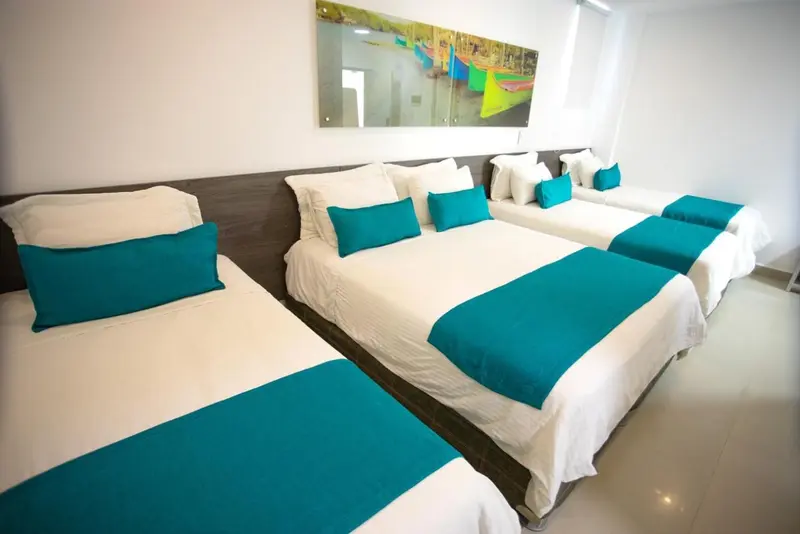 Une chambre lumineuse avec plusieurs lits blancs et des coussins turquoise.